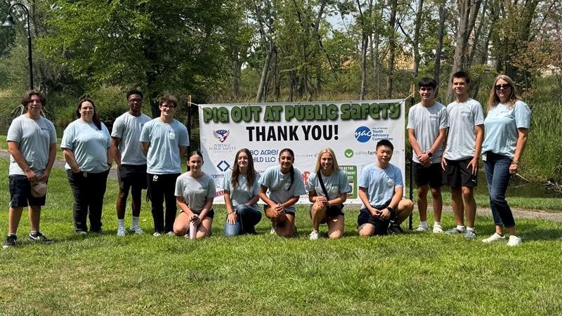 YAC Members standing and kneeling next to a Pig Out for Public Safety Banner